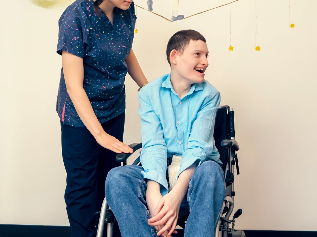 A caregiver supporting a smiling student who uses a wheelchair